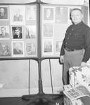 Fred Hartley standing in front of photos by Ace (Armando) Alagna, 1925-2000