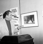 Eugenio Fernandi pointing to photograph on wall by Ace (Armando) Alagna, 1925-2000